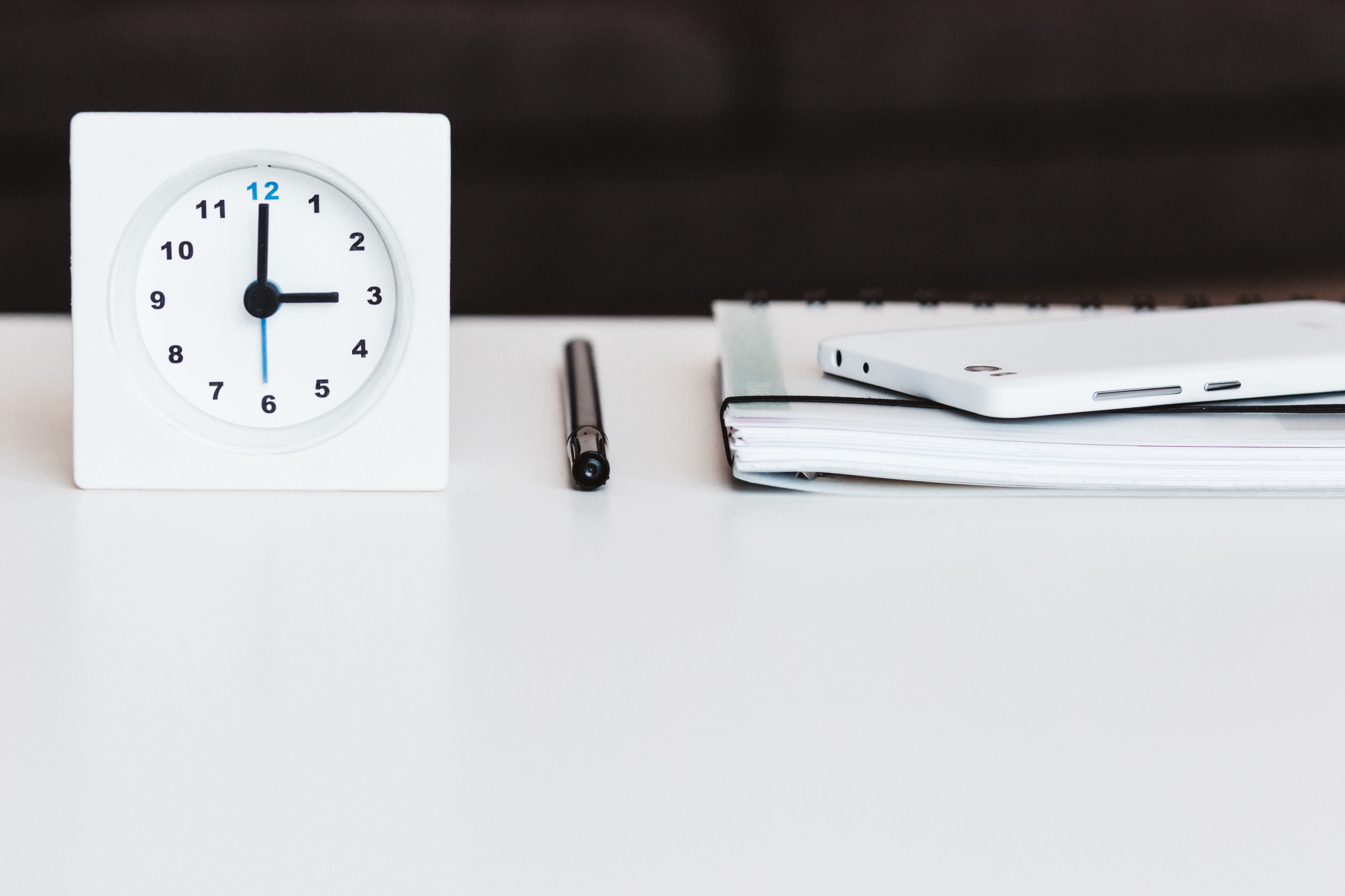 A clock, a pencil, and a planner rest on a table.